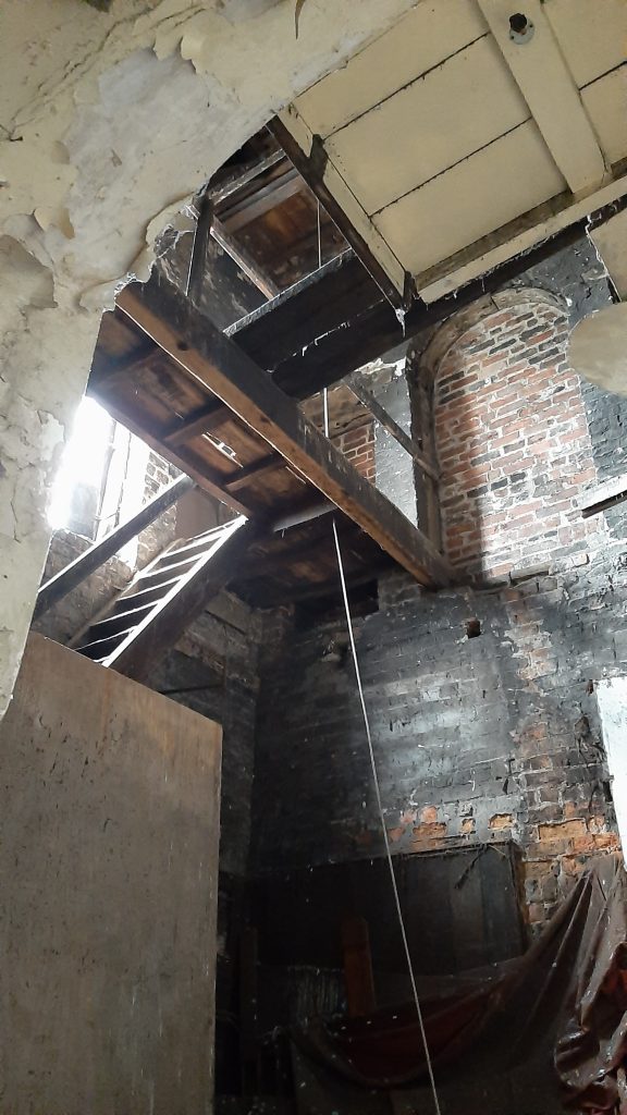Viw from the top of the first flight of stairs. A large chamber with wooden steps to the next level, bell rope and wooden gangways above.