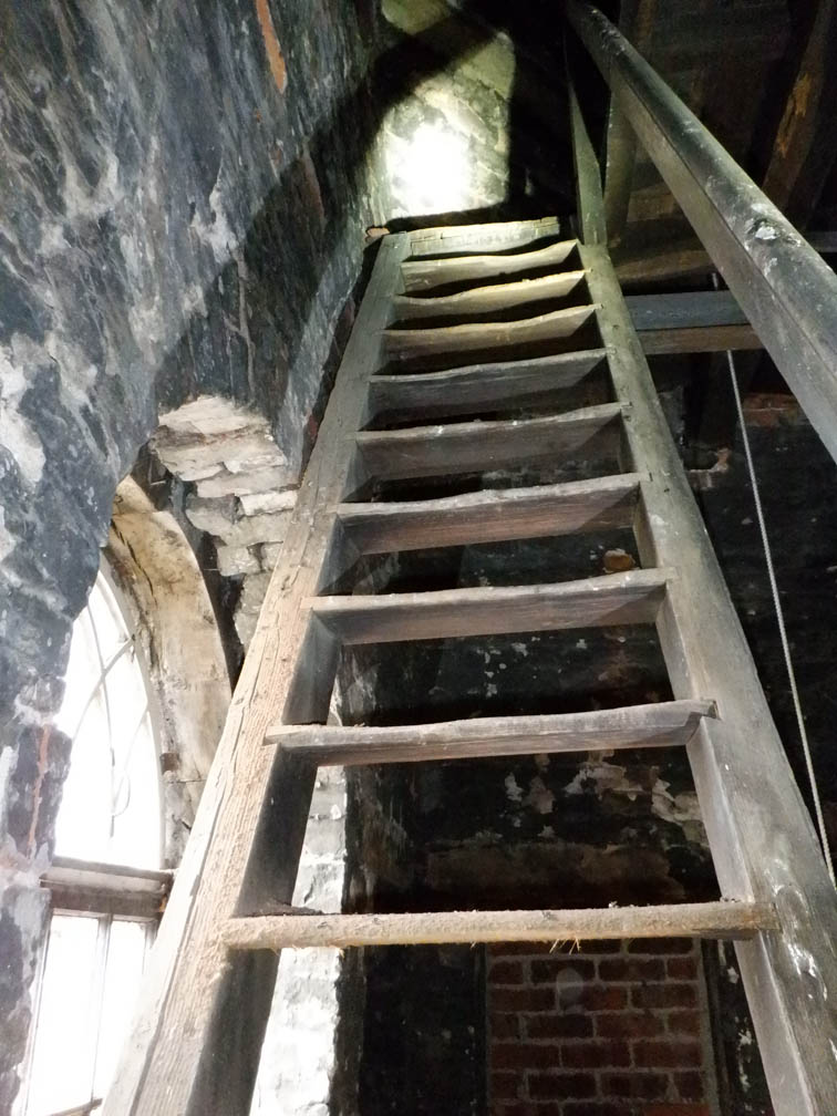 Wooden steps reach past the tip of an arched window up to another level in the tower