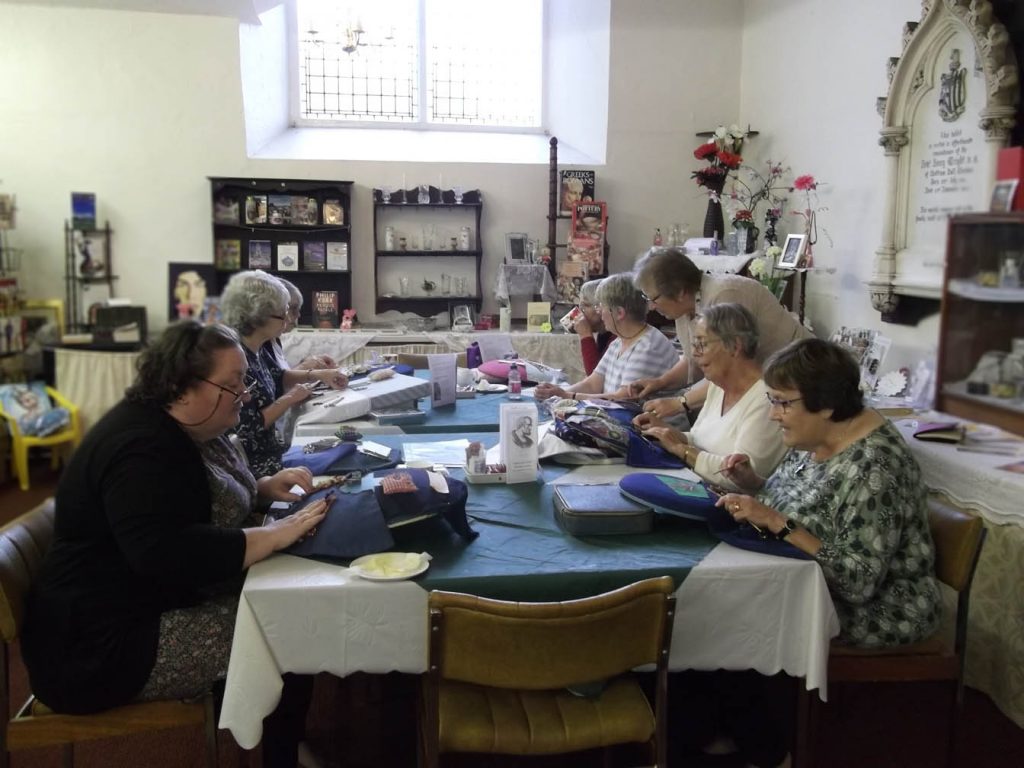 8 ladies busy making lace with the teacher stood giving assistance to one.